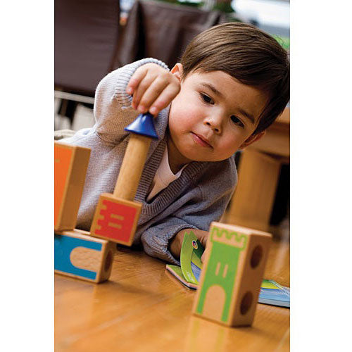 A young child engaged in play with Castle Logix, a mechanical puzzle by SmartGames. The child is carefully stacking colorful building blocks with a focus on a tower piece. The scene features a wooden floor and other game elements in the background, highlighting the fun and educational aspects of the toy.