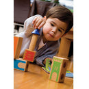 A young child engaged in play with Castle Logix, a mechanical puzzle by SmartGames. The child is carefully stacking colorful building blocks with a focus on a tower piece. The scene features a wooden floor and other game elements in the background, highlighting the fun and educational aspects of the toy.