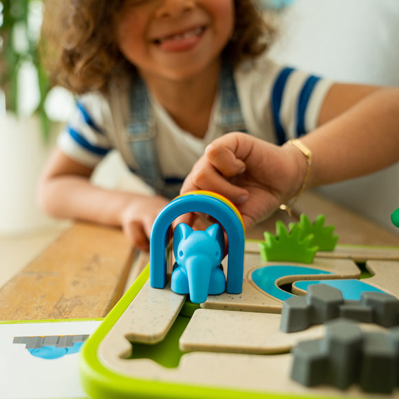 A child engages with the Safari Park Jr. mechanical puzzle by Smart Toys & Games. The colorful puzzle features an elephant figure under a rainbow arch, surrounded by green elements and gray shapes, stimulating creativity and problem-solving skills.