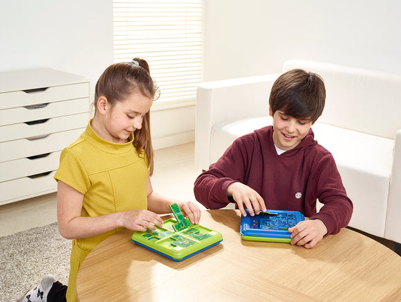 Two children engage in the Jungle Hide & Seek mechanical puzzle by SmartGames. One child is using a green puzzle while the other is focused on a blue one, both concentrating as they navigate through their challenges at a table in a bright room.