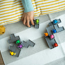 A child's hand placing colorful mechanical puzzle pieces on a striped rug. The pieces are gray with a textured design and feature bright animal figures in various colors, enhancing the playful atmosphere of building and creativity.