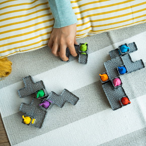 A child's hand placing colorful mechanical puzzle pieces on a striped rug. The pieces are gray with a textured design and feature bright animal figures in various colors, enhancing the playful atmosphere of building and creativity.