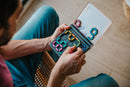 A person holding the IQ Digits mechanical puzzle by Smart Toys and Games, showcasing colorful, interlocking pieces arranged inside a transparent carrying case. The puzzle encourages logical thinking and problem-solving skills.