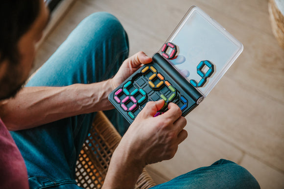 A person holding the IQ Digits mechanical puzzle by Smart Toys and Games, showcasing colorful, interlocking pieces arranged inside a transparent carrying case. The puzzle encourages logical thinking and problem-solving skills.