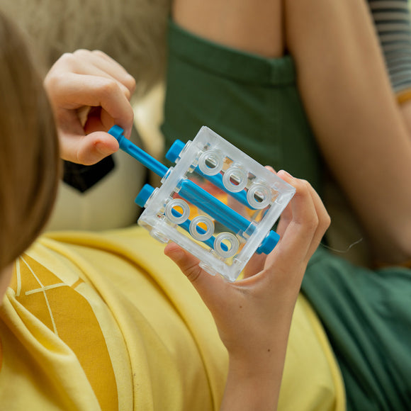 A child holding the Criss Cross Cube, a transparent mechanical puzzle featuring colorful, movable components. The child is focused on manipulating the puzzle, showcasing fine motor skills and problem-solving abilities.