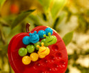 A colorful mechanical puzzle named Apple Twist from Smart Toys & Games. Features a bright red apple shape with various holes and six playful insect-like pieces in blue, green, yellow, and orange. The puzzle encourages problem-solving and fine motor skills for children.