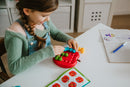 A child playing with the Apple Twist mechanical puzzle by Smart Toys & Games. The puzzle has colorful pieces in the shape of an apple, designed to enhance cognitive skills and hand-eye coordination. The child appears focused and engaged while placing the pieces into the puzzle. A book with illustrated instructions is placed nearby, promoting creative problem-solving.