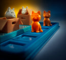 A colorful mechanical puzzle titled 'Cats & Boxes' by Smart Toys & Games, featuring three cat figurines in various colors positioned around small boxes on a blue base. The cats have distinct facial expressions, and the scene is illuminated softly, creating an engaging atmosphere.