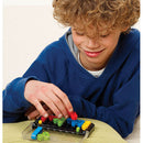 A young boy with curly hair is focused on solving the IQ Twist multi-level logic puzzle. He is placing colorful pieces onto a black puzzle board, showcasing concentration and enjoyment. The game features vibrant green, yellow, red, and blue pieces interlocked in a mechanical design, ideal for enhancing logical thinking skills.