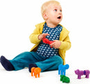 A young child sitting on the floor, interacting with colorful safari animal toys. The child is holding a red toy and surrounded by orange, green, purple, and blue animal figures. He has short blond hair and wide eyes, dressed in a fish-patterned shirt and a yellow zip-up hoodie, adding a playful vibe to the scene.