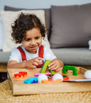 A young child with curly hair is engaged in play with Smartmax My First Acrobats. The child is stacking colorful magnetic shapes and figures on a wooden tray, showcasing bright colors and interactive design meant for early childhood development.