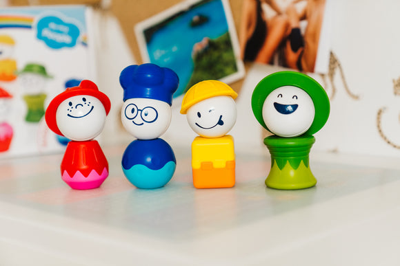 SMARTMAX My First People DIY kit featuring four colorful, friendly character figures. The characters include a smiling, red-hatted person, a blue-capped chef with glasses, a yellow-hatted construction worker, and a happy, green-hatted figure. These durable figures are designed for little hands, encouraging imaginative play and motor skills development.