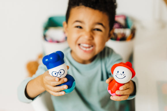 A happy child holding two colorful toy figures from the SMARTMAX My First People set. The toys are designed for young children, featuring cheerful faces and bright colors, promoting imaginative play and motor skills development. The child is engaging with the toys, showcasing a joyful expression.