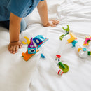 A child playing with the Smartmax Roboflex Large toy set on a light-colored fabric surface. The colorful pieces include a whimsical character with a blue head, yellow claws, and multiple flexible tubes connecting to various connectors and shapes. The arrangement encourages creative assembly and imaginative play for young children.