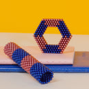 SPEKS Stripes Jellyfish, a colorful and unique mechanical puzzle composed of magnetic beads. Features a hexagonal shape and a tube, both displaying vibrant blue and copper colors, set against a bright yellow background.