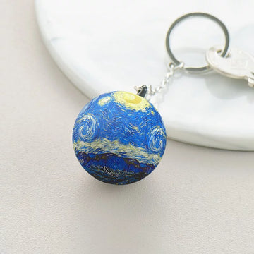 Vincent van Gogh - Starry Night Puzzle Keychain by Pintoo, featuring a spherical jigsaw puzzle design with vibrant blue and yellow colors inspired by the iconic painting. The keychain is attached to a silver chain, resting on a smooth white surface.