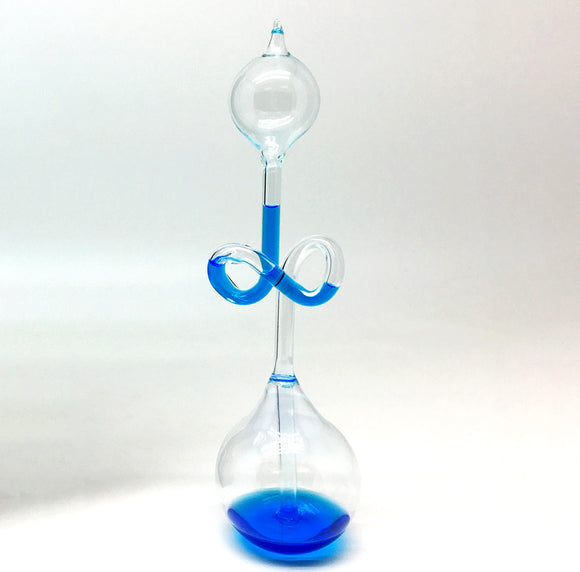 A clear glass hand boiler demonstration toy by Tedco. The apparatus features a bulbous base filled with blue liquid, a twisted tube, and a spherical top. As the user's hand warms the lower part, the liquid rises through the tube, showcasing a captivating physics phenomenon.