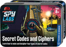 Spy Labs: Secret Codes and Ciphers kit by Thames & Kosmos, featuring a colorful tin package. The design shows a mysterious character using a code wheel, surrounded by urban scenery with palm trees, conveying an adventurous theme. Suitable for ages 8 and up, this educational kit teaches how to create and decode various secret codes.