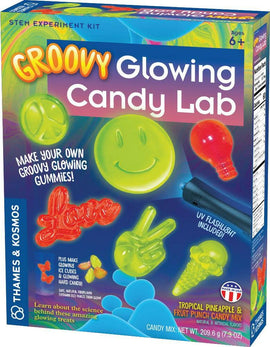 The Groovy Glowing Candy Lab by Thames & Kosmos is a vibrant DIY kit that allows kids ages 6 and up to create their own glowing gummy candies. The box features colorful images of various gummy shapes like a smiley face, peace sign, and heart, along with a UV flashlight included for illuminating the finished treats. It emphasizes a fun and educational approach to science with themes of candy-making and creativity.