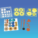 Orbiting Solar System Build Kit featuring various colorful components such as planetary discs, gears, and supporting structures designed for a DIY solar system model. The kit includes multiple pieces in bright colors, including white, yellow, and orange, along with a printed sheet displaying planet images.