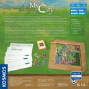 An overview of the board game 'My City' by Thames & Kosmos, featuring two-sided game boards, playing pieces, construction cards, envelopes, and the rulebook. The game revolves around urban planning and legacy mechanics, allowing players to build and develop their city through multiple episodes, with dynamic choices that impact future gameplay.