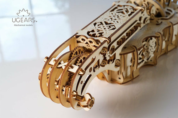 Close-up view of the UGears 3D Hurdy-Gurdy DIY kit, showcasing intricate wooden gears and decorative elements. The model features a stylized design with detailed engravings and multiple moving parts, demonstrating its mechanical complexity and artistic craftsmanship.
