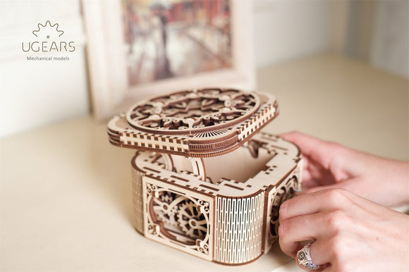 UGears 3D Treasure Box DIY kit showcasing an intricately designed mechanical wooden treasure box with detailed cutouts and a beautifully crafted lid being opened by a person. The treasure box features gears and precision engineering, perfect for both display and functionality.
