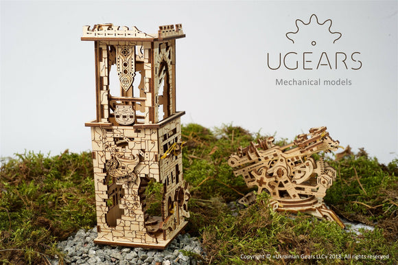The UGears 3D Archballista-Tower, a detailed DIY mechanical kit featuring intricately designed wooden pieces. The tower has a mix of architectural elements with a beautifully decorated façade, displayed among moss and rocks, capturing a unique blend of creativity and engineering.