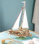 A beautifully crafted UGears 3D Trimaran Merihobus model displayed on a map. The wooden model sailboat features intricate details, including sails, rigging, and hull structure, showcasing an elegant design suitable for DIY enthusiasts and hobbyists. The scene includes a rope and instruction manual, adding to the nautical theme.