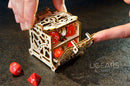 A person is using their finger to open the intricate wooden UGears 3D Dice Keeper. The elegant design showcases its compartments filled with vibrant red dice, while additional dice are placed on a dark surface nearby.