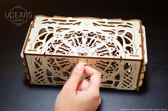 A detailed wooden card holder from UGears 3D, showcasing intricate cut-out designs. A hand is assembling the modular pieces, highlighting its DIY nature. The card holder sits on a dark wooden surface, emphasizing its craftsmanship.