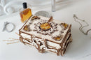A beautifully crafted UGears 3D Amber Box DIY kit, featuring intricate wooden designs and amber-like beads. The box is shown on a white surface alongside a perfume bottle and metallic circular objects, showcasing its elegance and detail.