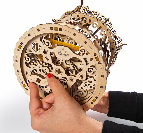 A person holds a beautifully crafted Ugears 3D Carousel mechanical model. The intricate design features decorative wooden gears and components, showcasing the artistry of the DIY kit. The carousel model is partially assembled, emphasizing the engaging and hands-on nature of this mechanical puzzle.