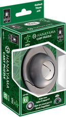 The Cast UFO mechanical puzzle by Hanayama features a sleek, silver design with a circular UFO shape. The packaging highlights its complexity, rated level 6, and invites users to take it apart and reassemble it. The box is green with bamboo patterns and includes text encouraging users to collect them all.