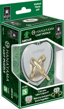 The Cast Amour mechanical puzzle by Hanayama features a heart-shaped design with intricate loops made of metallic materials. The packaging displays the product name and level 5 difficulty, inviting users to take it apart and reassemble it. The vibrant green box includes a spider logo and encourages collectors with phrases like 'Collect Them All!'