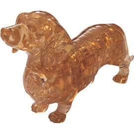 A 3D crystal jigsaw puzzle shaped like a dachshund made by bePuzzled. The crystal dachshund features a translucent amber color with intricate detailing that highlights its unique shape and texture. It stands upright, showcasing a playful expression, making it a charming addition to any puzzle collection.