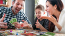 A family enjoying a game of Clue by Winning Moves. The scene shows a man and woman smiling and excitedly playing along with a young boy. Colorful game pieces and cards are visible on the table, creating a lively and engaging atmosphere.